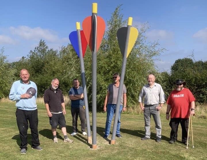 Men in sheds volunteers standing around an arrows sculpture they built